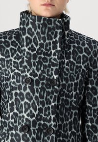 Manteau en imprimé léopard avec un col haut, fabriqué en tissu doux. Présente des boutons noirs et une conception structurée dans des tons de gris et de noir.