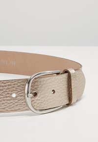 Ceinture en cuir beige avec une finition texturée, boucle en métal argenté, et plusieurs trous pour ajustement. Doublure intérieure lisse pour le confort.