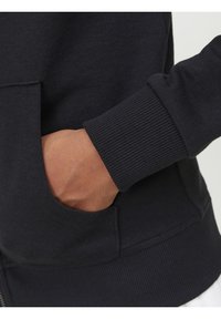 Zwart sweatshirt met een geribbelde manchette en een voorzak. De stof lijkt zacht en rekbaar, wat zorgt voor comfortabele draagbaarheid.