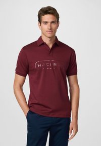 Burgundská polo košile s límečkem a krátkým rukávem, s velkým, reliéfním logem na přední straně. Hladká textilie, jednoduchý design.
