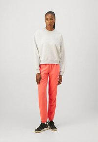 Grå genser og korallfargede joggebukser, begge med myk tekstur. Svarte joggesko med enkel design og synlig logodetalj på buksene.