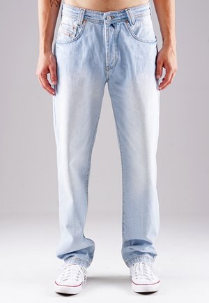 Helle blaue Jeans mit einer lockeren Passform, geradem Bein, fünf Taschen und kupferfarbenen Nieten. Getragen mit weißen Sneakers.
