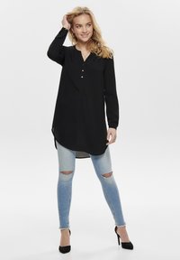Czarna tunika z długim rękawem, dekoltem w serek i detalami z guzikami, zestawiona z jasnoniebieskimi przetartymi skinny jeansami i czarnymi szpilkami.