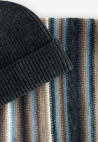 Knitted black beanie atop a striped scarf featuring brown, blue, and cream lines. The scarf has a soft texture with varied thickness.