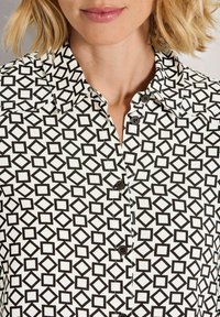 Black and white button-up shirt featuring a geometric square pattern, collared design, and black buttons. Fabric appears smooth and lightweight.