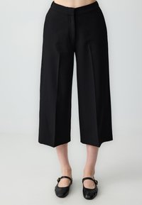 Pantalons noirs cropped en tissu lisse, avec une coupe droite, des poches latérales discrètes et une taille structurée.