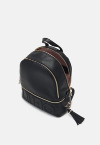 Schwarzer Leder-Rucksack mit goldenen Reißverschlussakzenten, runder Form und strukturiertem Finish. Mit einem Logo auf der Vorderseite und einem Quasten-Detail.
