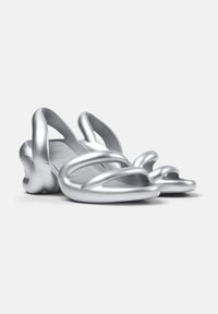 Silver sandals with a unique design featuring intertwined straps, smooth texture, and a contoured sole. Lightweight and modern shape.