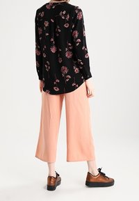 Svart blommig blus med långa ärmar och knappade manschetter, parat med lätta persikofärgade culotter och bruna snörskor.