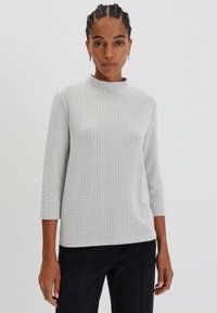 Haut gris clair à col montant avec des manches trois-quarts, motif en maille texturé et coupe décontractée, fabriqué à partir d'un matériau doux et extensible.