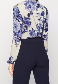 Blusa floreale con fiori blu e crema, maniche lunghe e una vestibilità ampia abbinata a leggings a coste blu navy scuro.