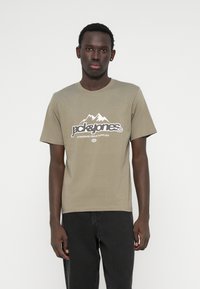 Olīvu zaļas krāsas kokvilnas T-kreklis ar apaļu kakla izgriezumu un īsām piedurknēm, uz kura krūtīm ir kalnu grafika un zīmola nosaukums baltā krāsā.