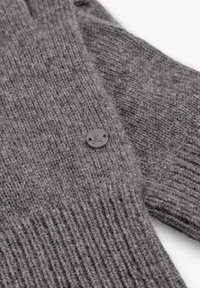 Suéter gris de punto con textura acanalada, patrón sutil y un botón negro redondo con diseño de calavera.