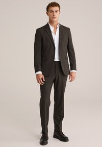 Mörkgrå kostym med skräddarsydd passform, som har en enkelknäppt jacka, snedskurna slag och matchande byxor. Vit skjorta under.