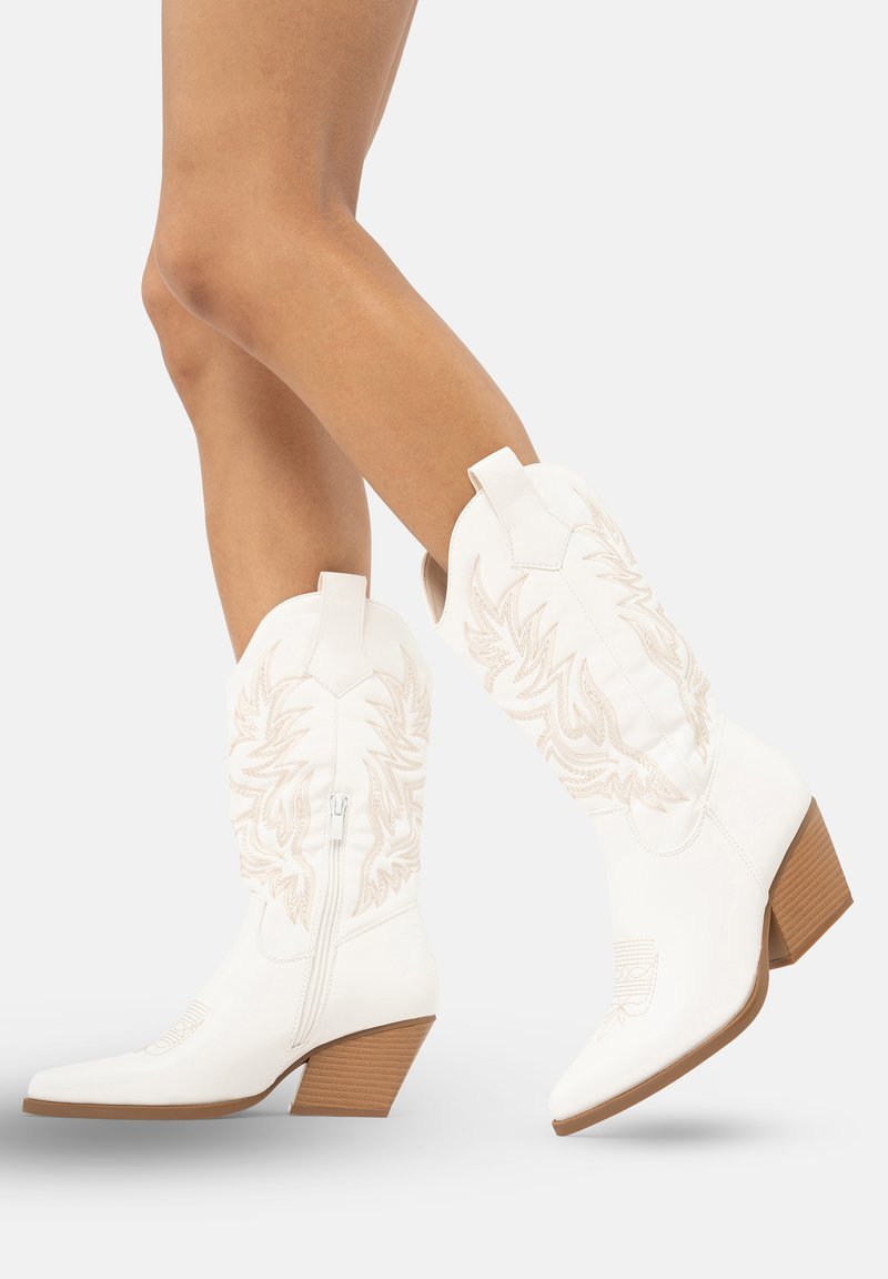 Botas de vaquero blancas con bordado sutil, punta afilada y un tacón apilado de 2 pulgadas. Incluyen una cremallera lateral y lengüetas para facilitar su uso.