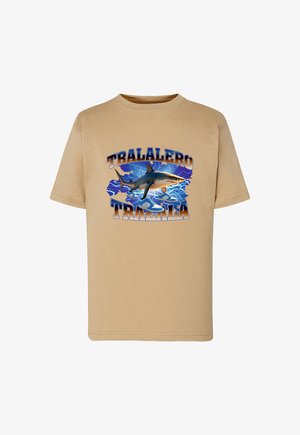 Beżowa bawełniana koszulka z kolorową grafiką rekina pośród niebieskich fal, z napisem "TRALALERO" u góry i "TRALALA" na dole.
