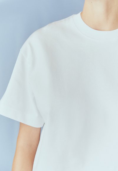 T-shirt bianco in cotone a maniche corte, con scollatura rotonda e texture liscia. Presenta una vestibilità rilassata e un design minimalista.