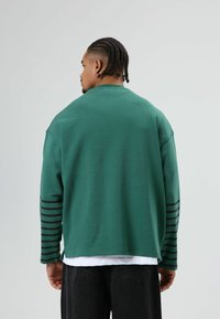 Groen sweatshirt van zacht materiaal met zwarte gestreepte accenten op de mouwen, een ontspannen pasvorm en een ronde hals.