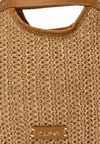 Bolso de paja tejido en color marrón con superficie texturizada, que cuenta con un asa de cuero en color marrón y un acento de logo dorado en la parte inferior.