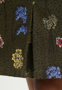 Tela con estampado floral sobre fondo verde oscuro, con flores azules, amarillas y rojas. Texturizada con pequeños puntos oscuros en toda su superficie.