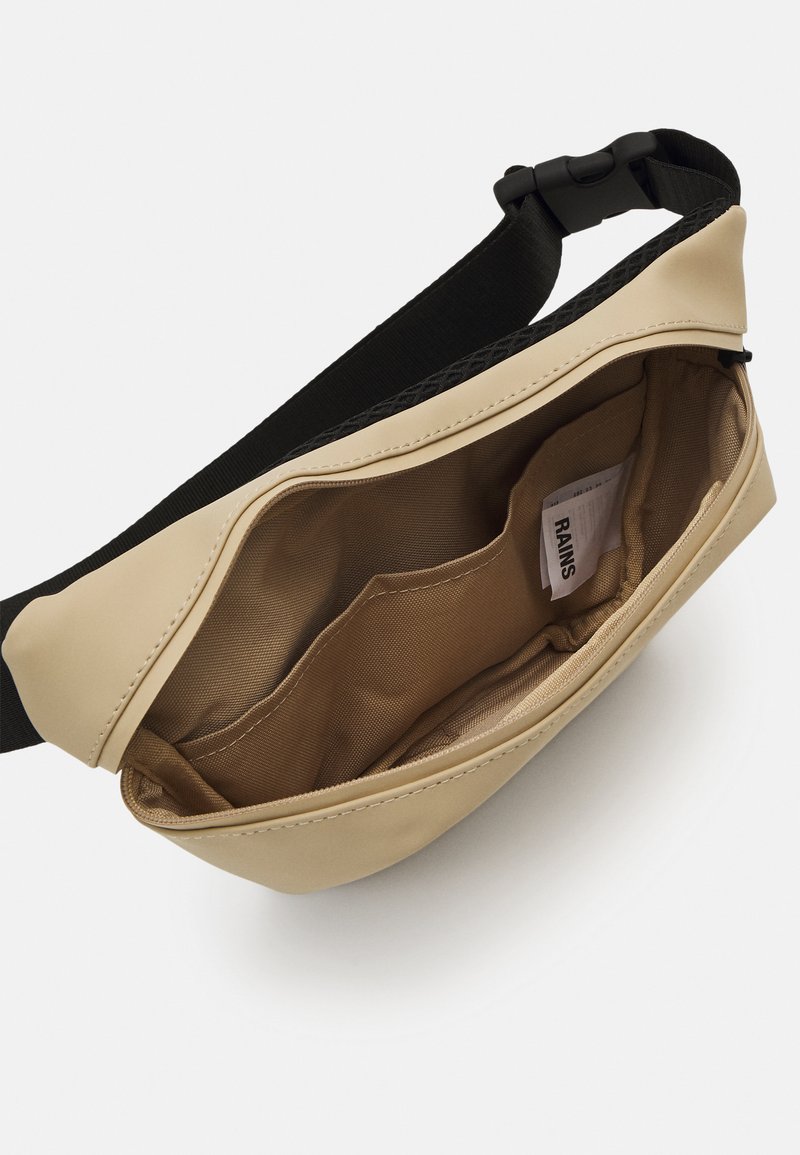 Sacoche beige imperméable à bandoulière avec un extérieur lisse, une sangle noire ajustable et un intérieur beige comportant plusieurs poches.