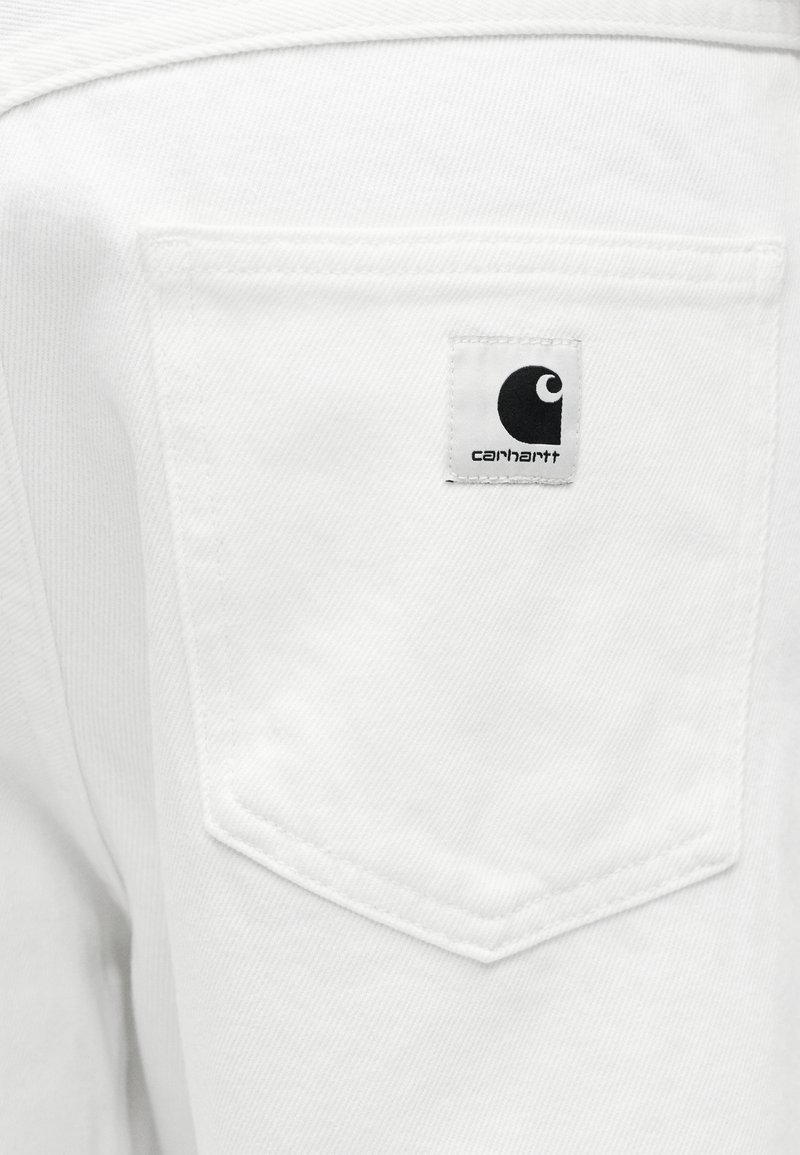 Tasca posteriore di pantaloni in denim bianco con toppa del logo Carhartt cucita in bianco e nero.