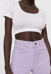 Top corto blanco acanalado con mangas cortas, combinado con jeans lavanda de cintura alta que cuentan con bolsillos delanteros y cierre de botón metálico.