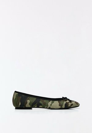 Chaussure de ballet plate avec motif camouflage vert et marron et petit nœud noir sur l’orteil sur fond blanc.