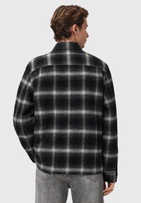 Camicia di flanella a quadri bianco e nero con una texture liscia, colletto visibile e polsini con bottoni. Design a vestibilità rilassata.