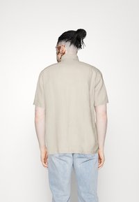 Korte mouwen, lichtbeige overhemd met een rechte kraag en een losse pasvorm, gemaakt van een gestructureerde stof, gecombineerd met lichtblauwe spijkerbroek.