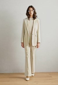 Puku comprises a striped blazer and flared trousers in pastel colors, paired with a light top and white block-heel shoes. Worn transparent glasses.