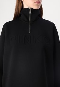 Pullover nero con colletto alto, dotato di una cerniera argentata e del logo "PINKO" in rilievo sulla parte anteriore. Tessuto morbido con una texture liscia.