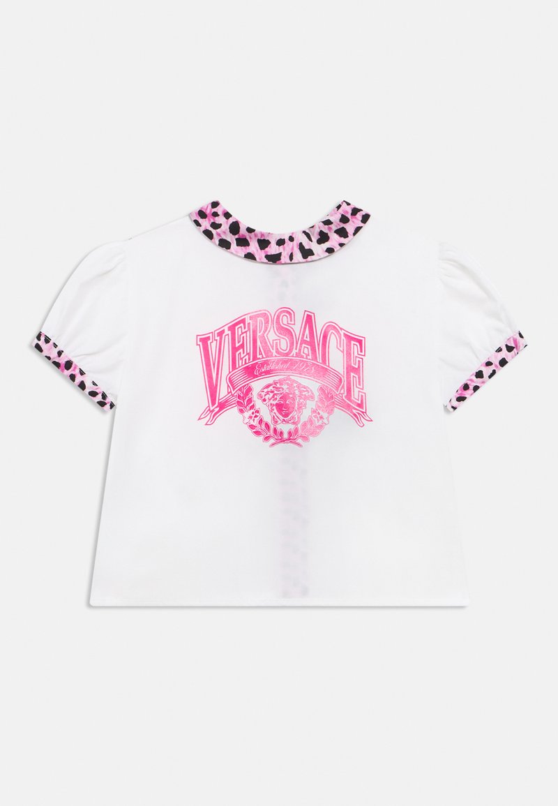 Λευκό τοπ με κοντά μανίκια, με γιακά και μανσέτες σε ροζ λεοπαρ σχέδιο, με λαμπερό ροζ λογότυπο Versace και έμβλημα κεφαλής Μέδουσας στο μπροστινό μέρος.