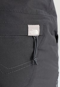 Svarta utomhusbyxor har en tygetikett med "The North Face"-logotyp, kontrasterande sömmar och en dragsko i bakfickan.