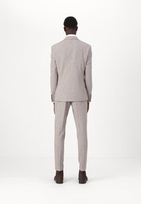 Fato cinza claro, ajustado, com um casaco estruturado e calças slim-fit. O tecido tem uma textura subtil. Sapatos castanhos completam o visual.