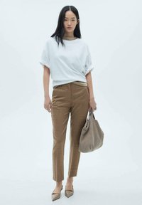 Bílé oversized tričko, hnědé kostkované kalhoty na míru, béžová kabelka a špičaté baleríny. Hladké materiály, světlá barevná paleta, uvolněný styl.