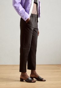 Lila kurzes Jacket, schwarze eng anliegende Hose und schwarze Mules mit offenem Zeh und niedrigem Absatz; glatte Texturen und maßgeschneiderte Designs sind sichtbar.