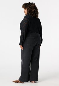 Zwarte doorzichtige blouse met bloemenstructuur, gecombineerd met hoge taille, wijde donkere jeans. Dierenprint puntige ballerina's maken de outfit compleet.