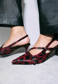 Red and black leopard print slingback heels with pointed toe, textured fur finish, and curved block heel; features cross-strap design with accents.