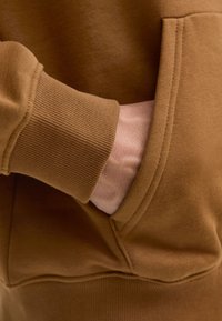 Brązowa bluza z kapturem z prążkowanymi mankietami i przednią kieszenią, wykonana z miękkiego materiału o gładkiej fakturze. Widoczne są przeszycia.