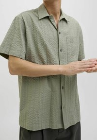Short-sleeve shirt in light green textured fabric, featuring a collar, button closure, and a chest pocket. Casual fit with a structured design.