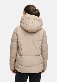 Beige puffer jacket met capuchon, met een gestikte ontwerp, ritsafsluitingen en een subtiele logo-detail op de achterkant. Zacht, textuurstof.