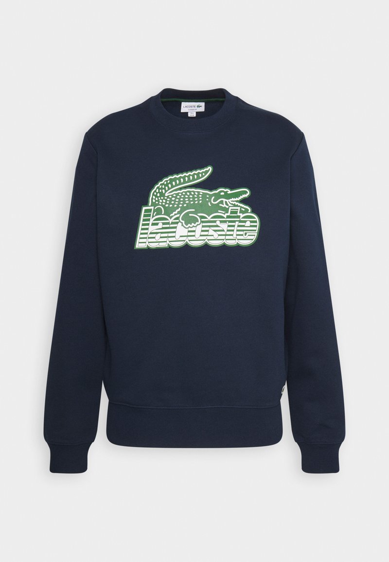 Sweatshirt bleu marine avec des poignets et un ourlet côtelés, présentant un grand logo Lacoste vert et blanc avec un alligator sur le devant.