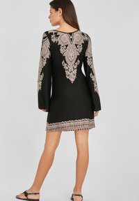 Vestido negro de manga larga, con intrincados bordados en rosa y dorado en el escote y el dobladillo. De corta longitud.