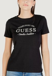 T-shirt in cotone nero con scollo rotondo, maniche corte e un logo stampato bianco con la scritta "GUESS" e "Established 1981".