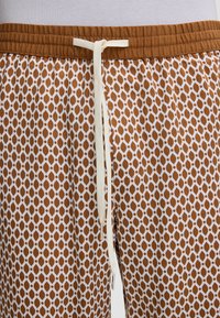Pantaloni a pattern marrone e bianco con vita elastica e cordino bianco annodato a fiocco al centro anteriore.