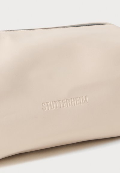Funda impermeable beige hecha de material suave, con un discreto logo en relieve y un cierre de cremallera en el borde superior.