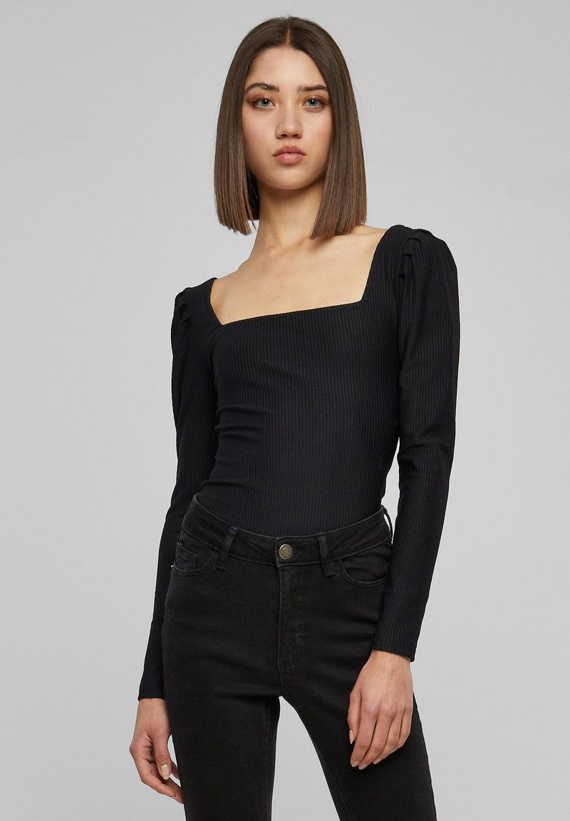 Svart ribbet bodysuit med firkantet utringning og puffede lange ermer, kombinert med høyhalsede svarte jeans. Glatt tekstur, tettsittende design.
