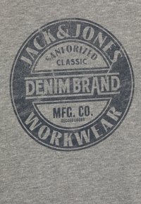 T-shirt in cotone grigio con una grande grafica circolare blu e il testo: "JACK & JONES SANFORIZED CLASSIC DENIM BRAND MFG. CO. RUGGED GOODS WORKWEAR."