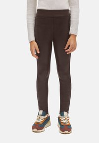 Leggings marrones en un diseño ajustado con una textura suave, combinados con zapatillas de cordones coloridas que presentan acentos multicolores.